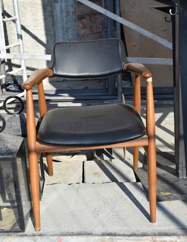 Mid-century modern wooden dining chair with black leather seat and backrest, minimalist design photographed outdoors. (Accent Leather Chairs)