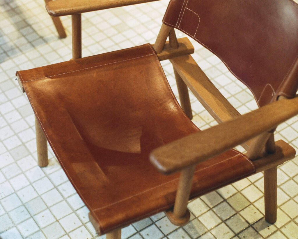 Brown leather sling chair with wooden frame, mid-century modern accent chair in minimalist interior setting. (Accent Leather Chairs)